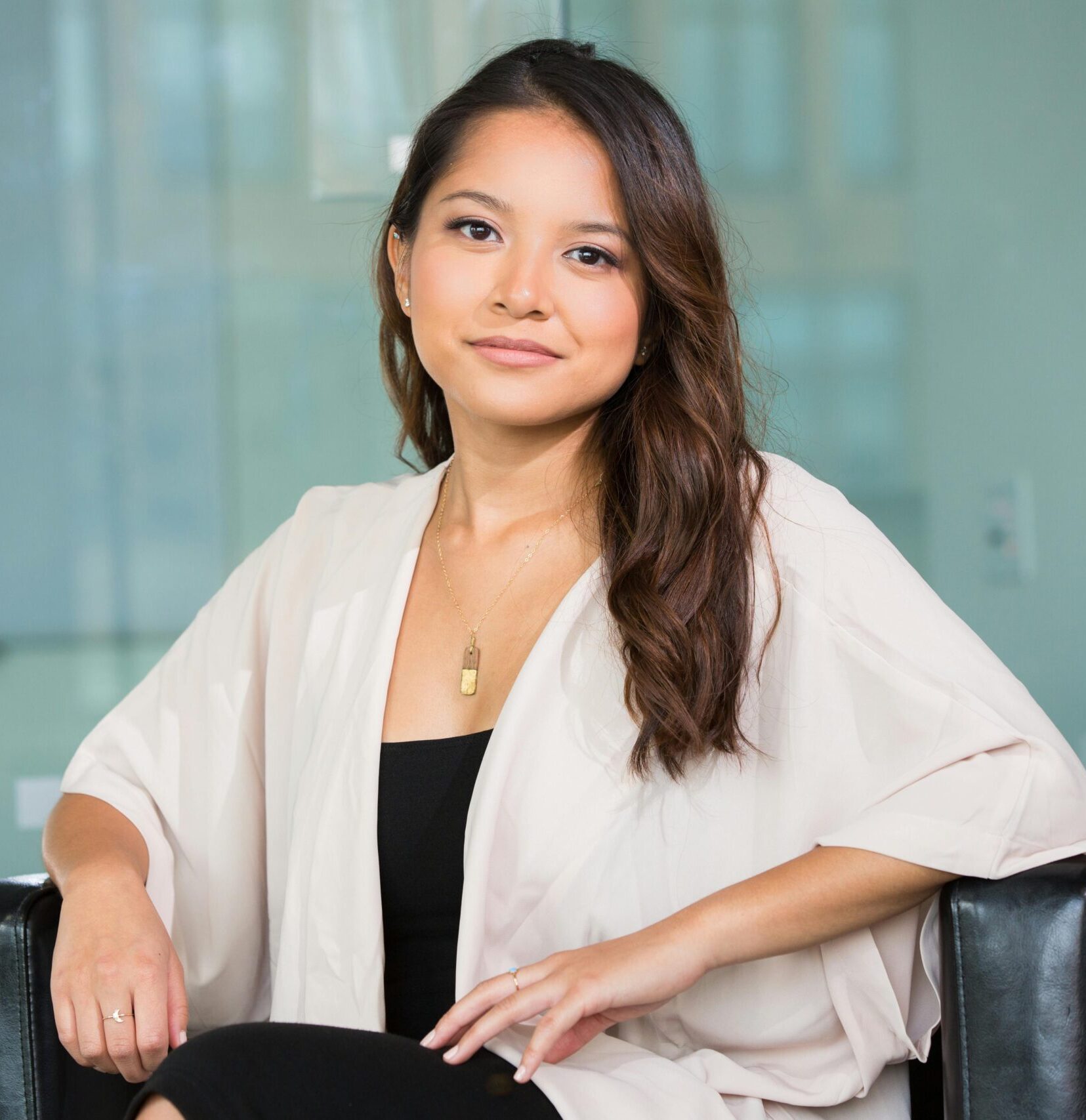 A professional Asian businesswoman sitting confidently in a modern office setting.