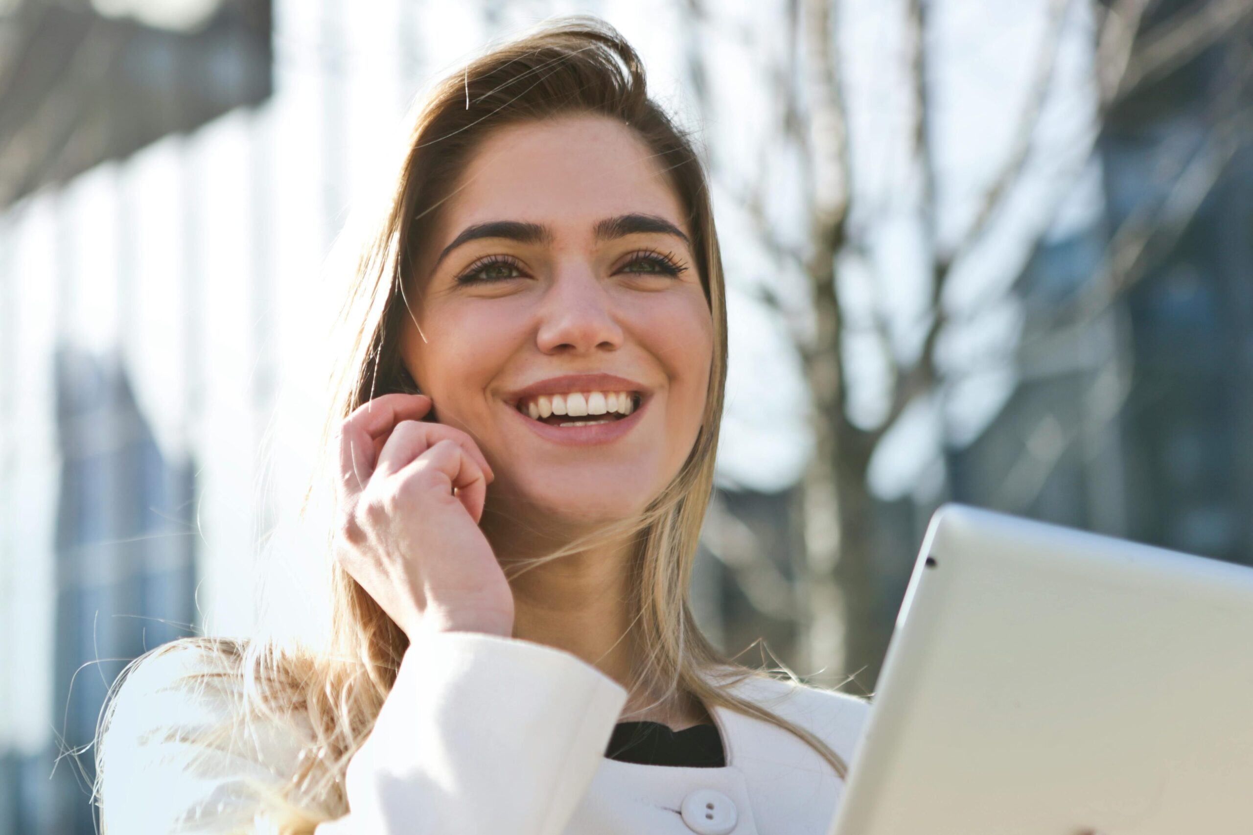 Confident businesswoman using her tablet and phone, smiling outdoors in sunlight.
